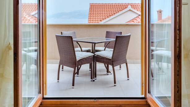 Varanda com mesa e cadeiras, vista de um telhado com telhas vermelhas e céu claro.