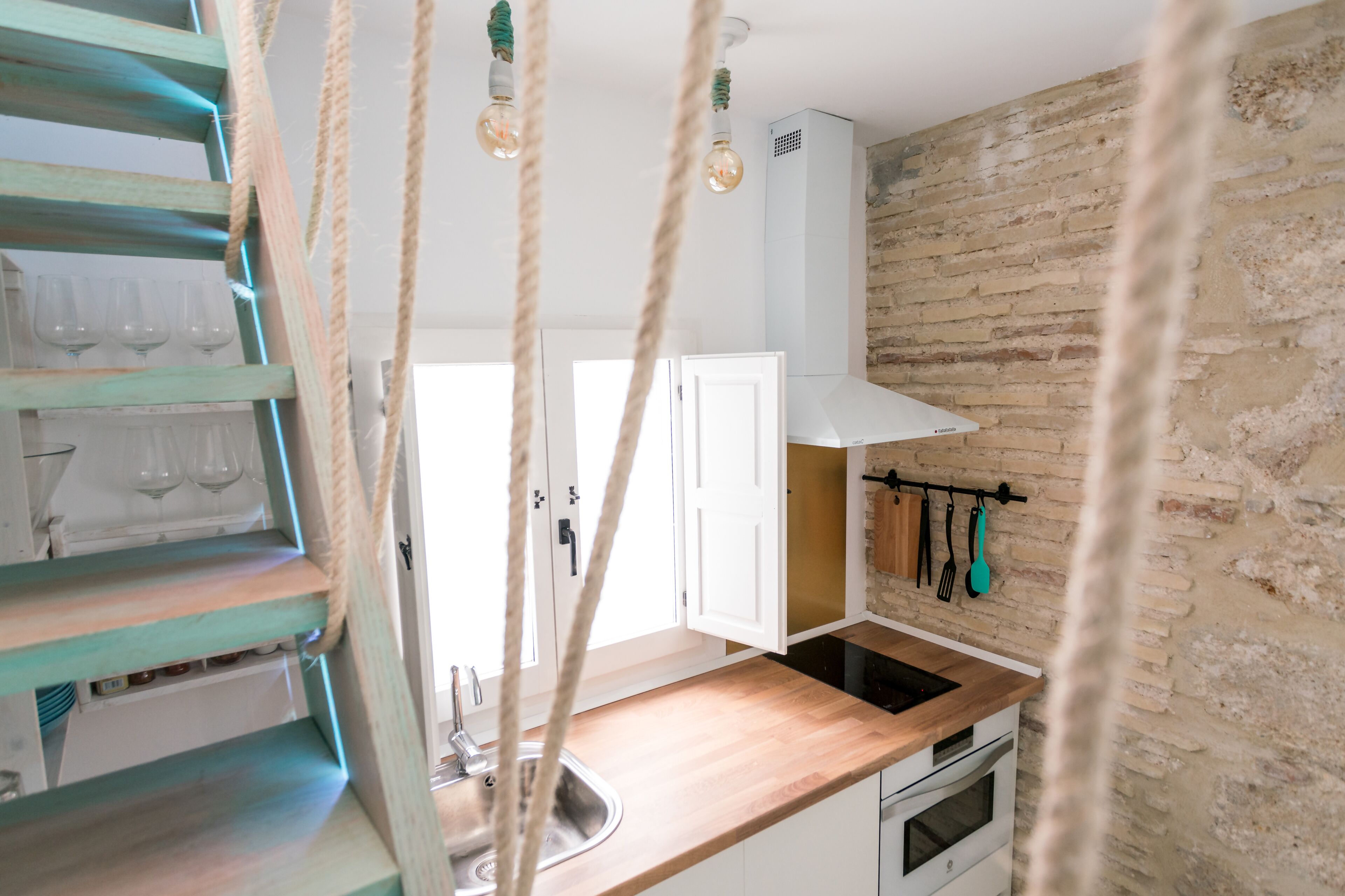 A kitchen with a wooden countertop, a stainless steel sink, and a hanging pot rack.