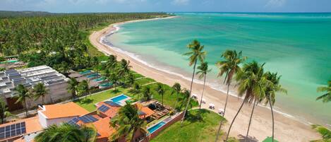 A coastal resort with a beach, palm trees, and a pool area.