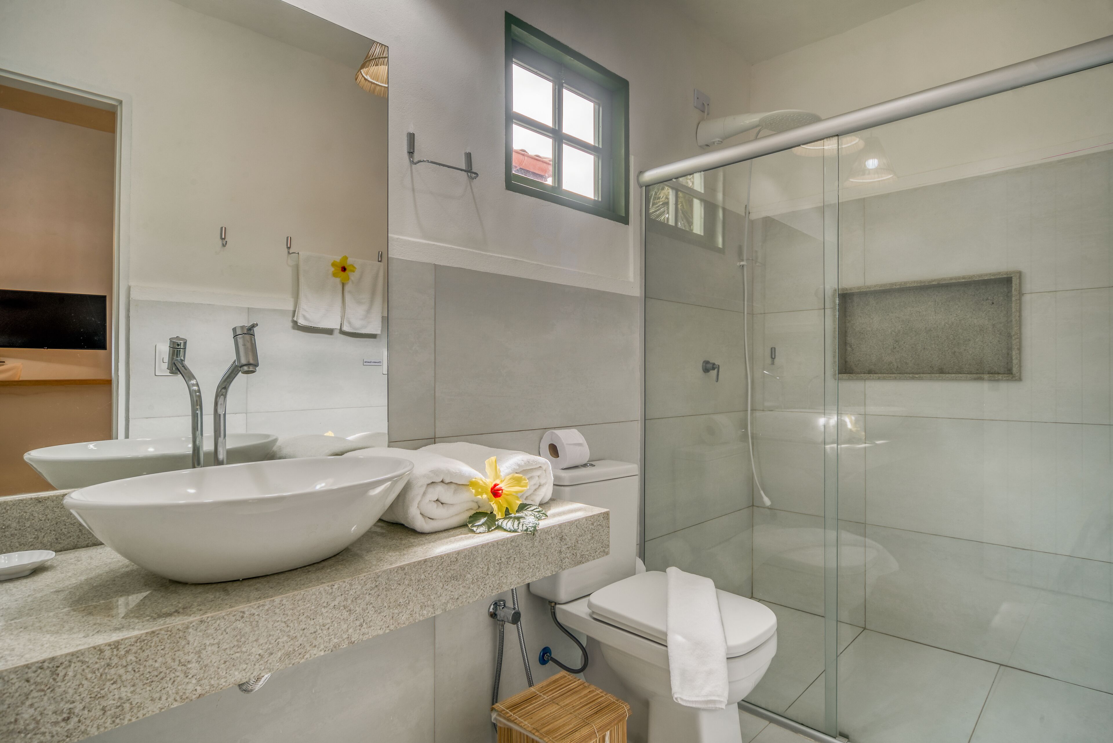 Een moderne badkamer met een groot wit wastafelmeubel, twee kraanwerkdelen, een toilet en een douchecabine met glazen wanden.