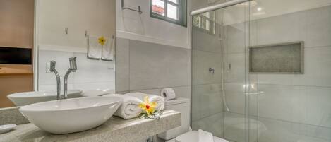 Un baño moderno con un lavamanos grande blanco, dos grifos, un inodoro y una ducha con mampara de vidrio.
