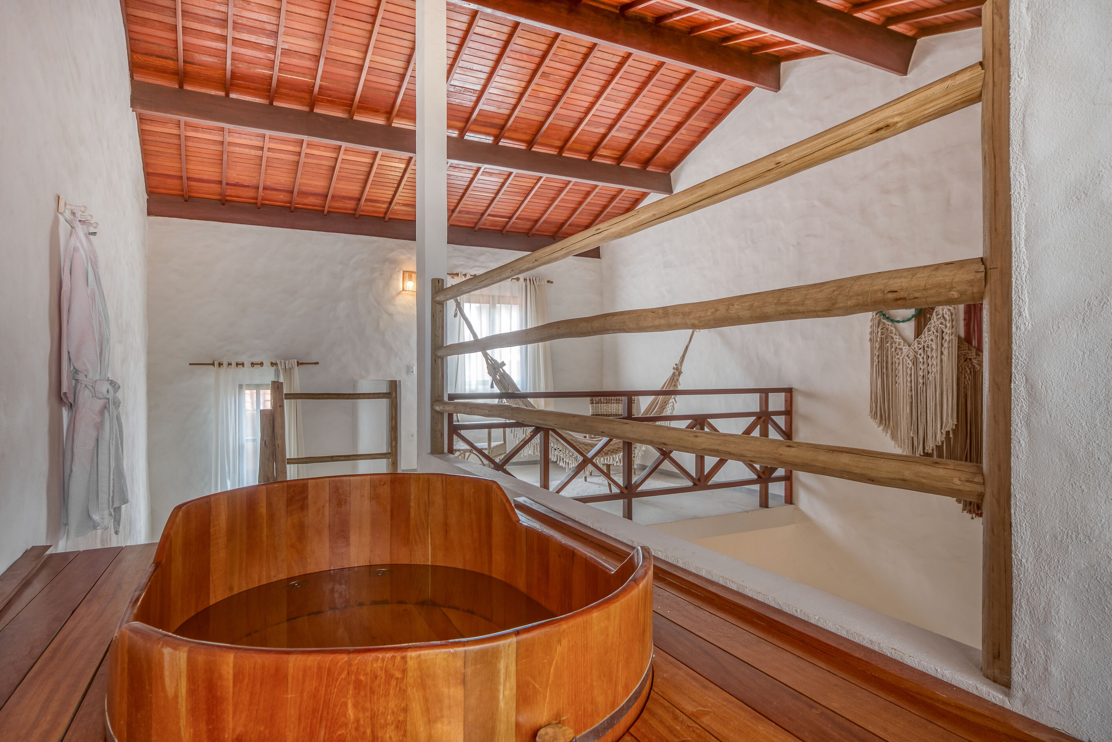 A wooden bathtub in a room with a high ceiling and wooden beams.