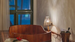 A wooden bathtub with a towel and a bottle, a lamp, and a window with a view of the sea. - Pousada Rota Ecológica (Porto de Pedras)