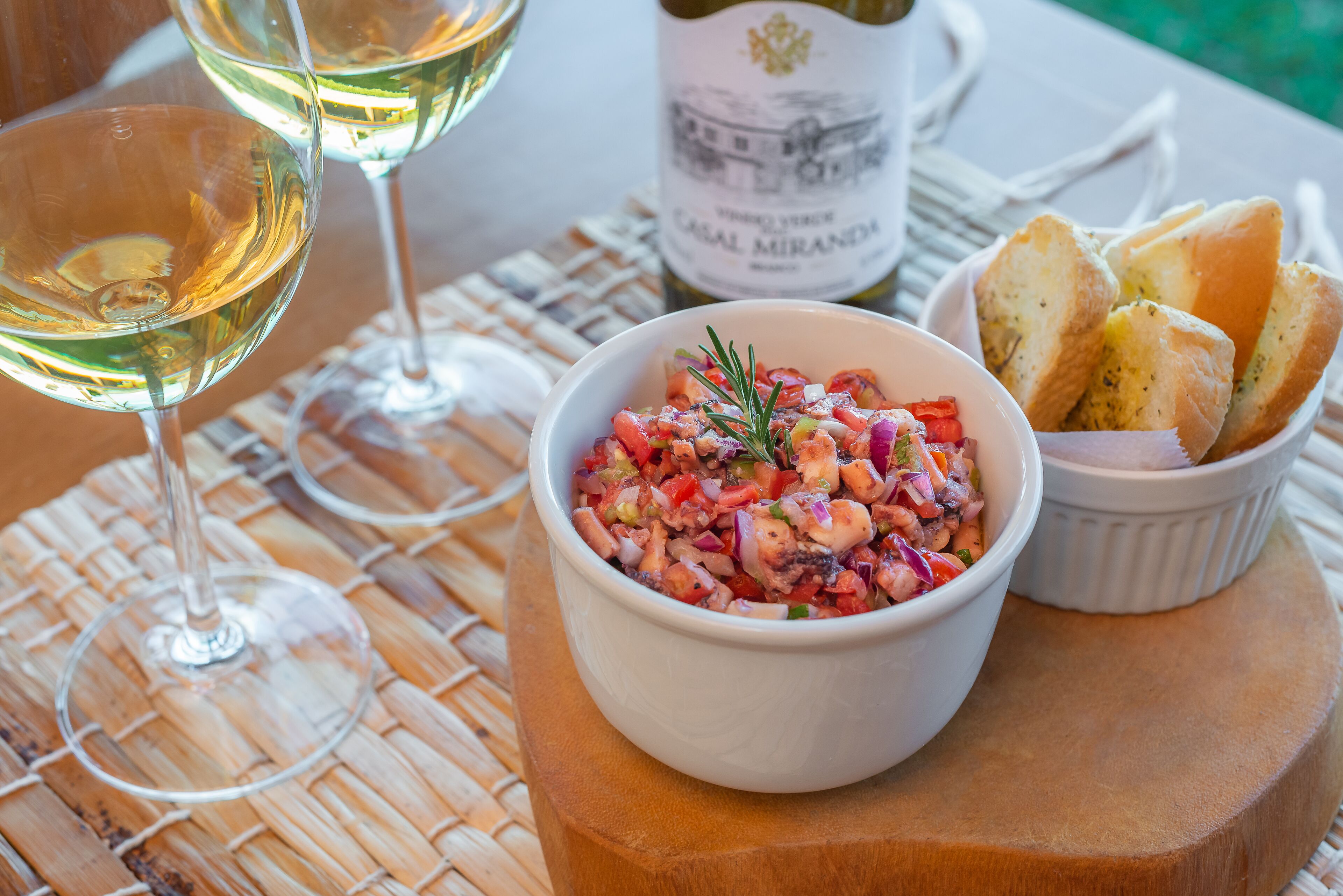 A table setting with a bowl of diced vegetables, a bottle of wine, and bread.