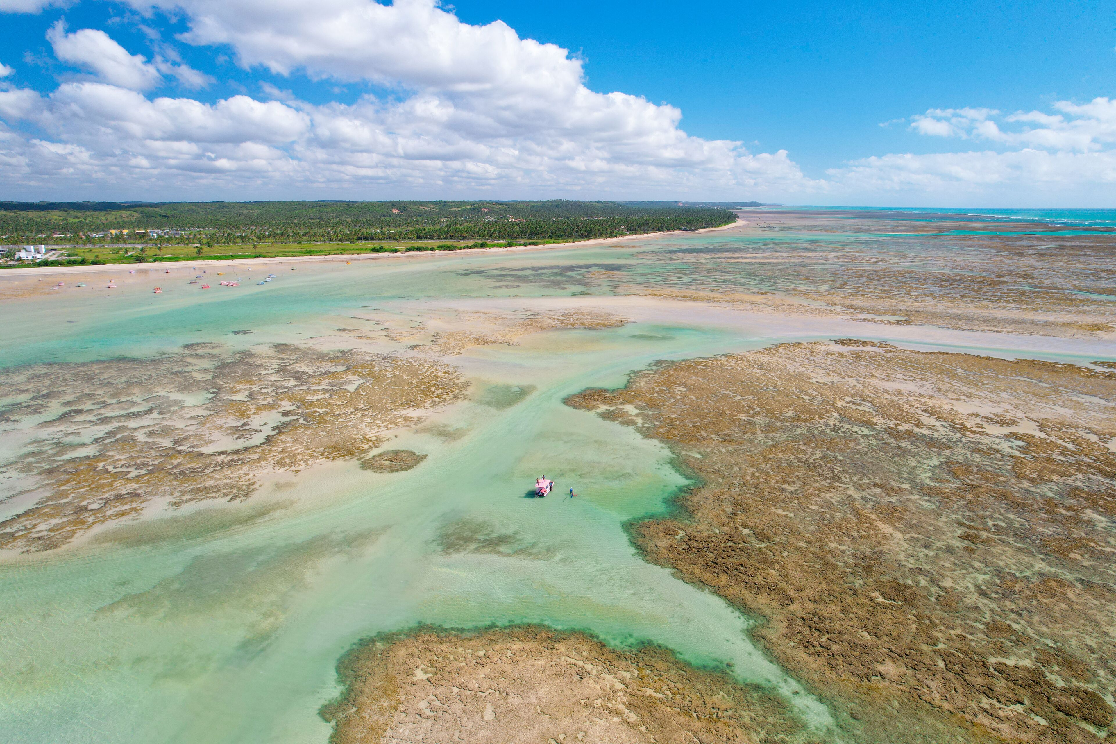 An aerial view of a coastal area with clear waters, sandy beaches, and a distant shoreline with vegetation.