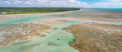 An aerial view of a coastal area with clear waters, sandy beaches, and a distant shoreline with vegetation.