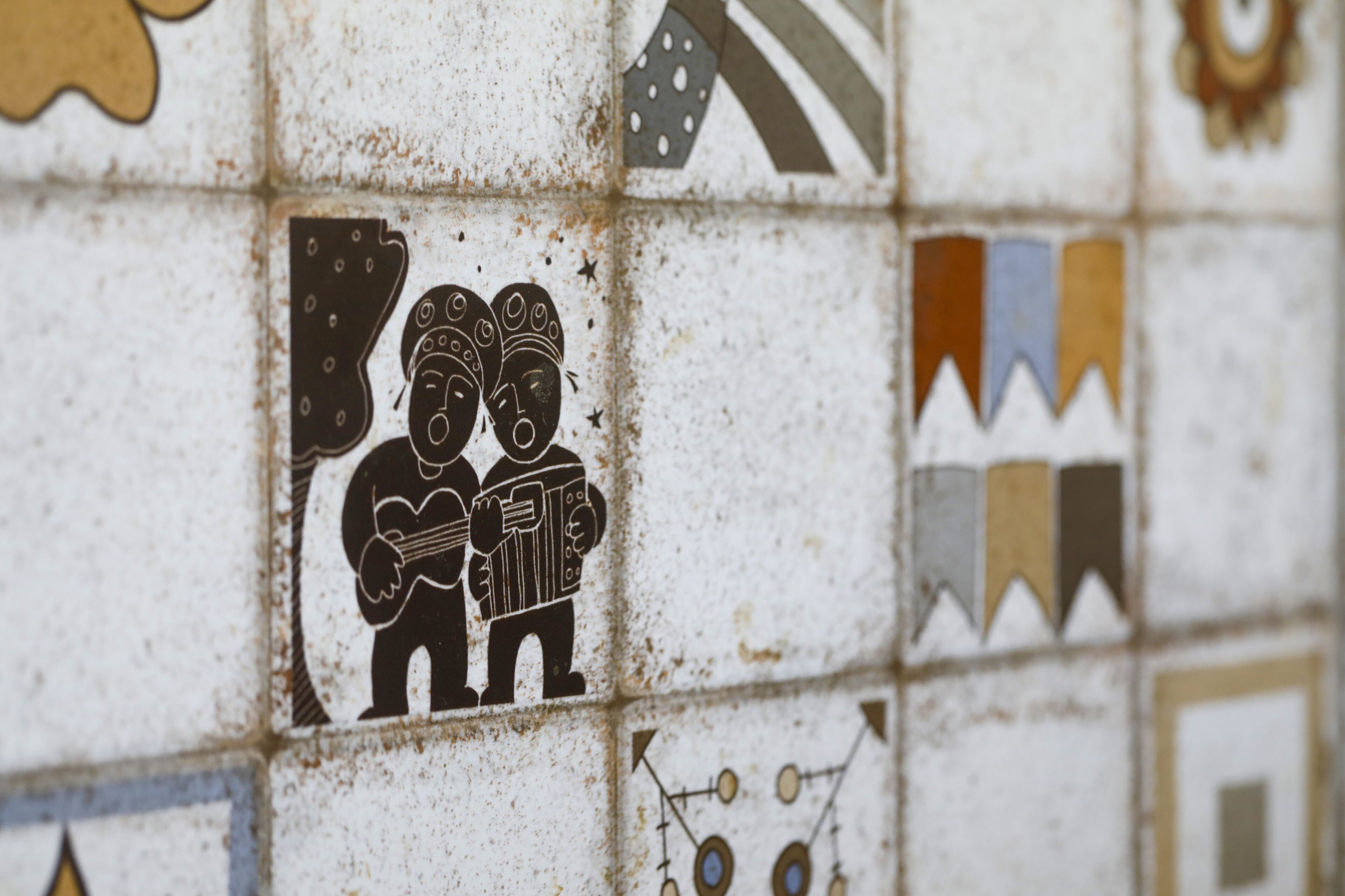 Primer plano de una pared de azulejos con diversos diseños y patrones, incluyendo una figura central tocando la guitarra.