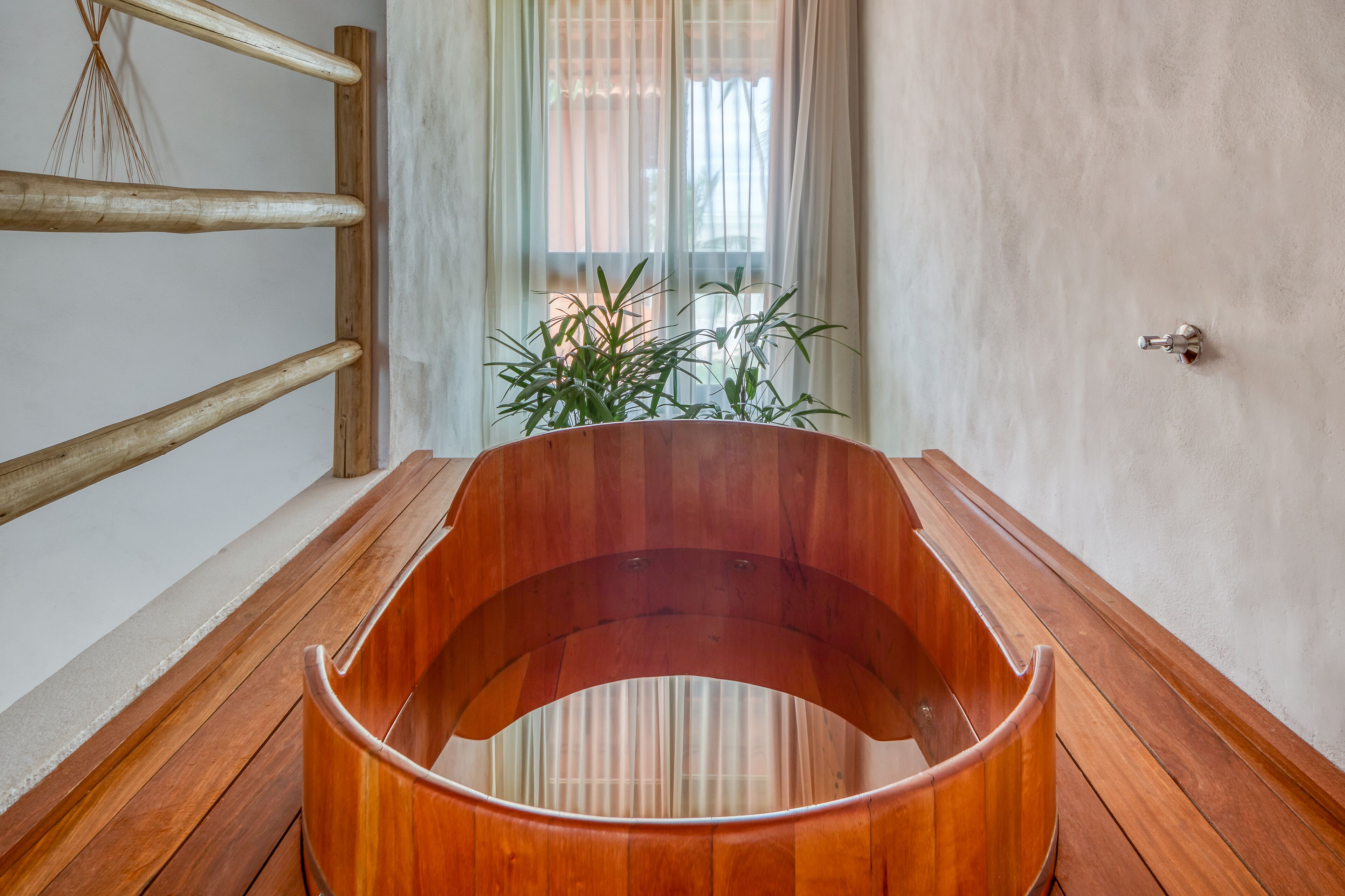 A wooden bathtub in a room with a wooden bench and a plant.