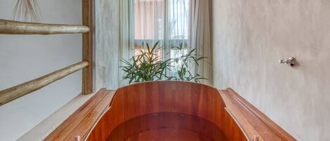 A wooden bathtub in a room with a wooden bench and a plant.