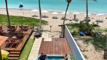 Zona de piscina con terraza de madera, sillas de descanso y vistas a la playa y al océano.