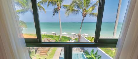 A room with a view of the ocean, two wicker chairs, a glass table, and a small plant.