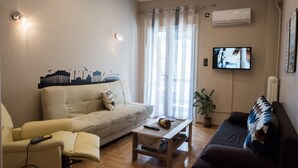 A living room with a beige sofa, a dark sofa, a wooden coffee table, and a television on the wall. - Gazi Divine Apartment (Athens)