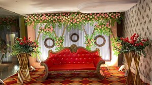 Ein rotes Sofa mit goldener Zierleiste in einem Raum mit gemustertem Teppich, dekorativen Spiegeln und floralen Arrangements.