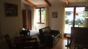 Una sala de estar acogedora con sofá, una mesa de comedor con sillas, una zona de cocina con estufa y ventanas amplias que dejan entrar luz natural.