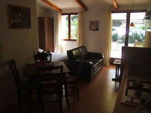 A cozy living area with a sofa, a dining table with chairs, a kitchen area with a stove, and large windows allowing natural light.