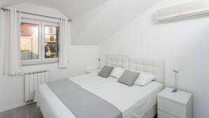 A modern bedroom with a large bed, white bedding, a nightstand with a lamp, and a window with curtains. - Apartments Villa Dubrovnik (Konavle)