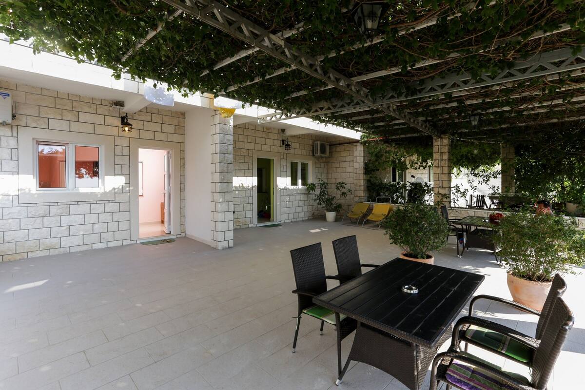 An outdoor patio area with a table and chairs, potted plants, and a pergola structure.
