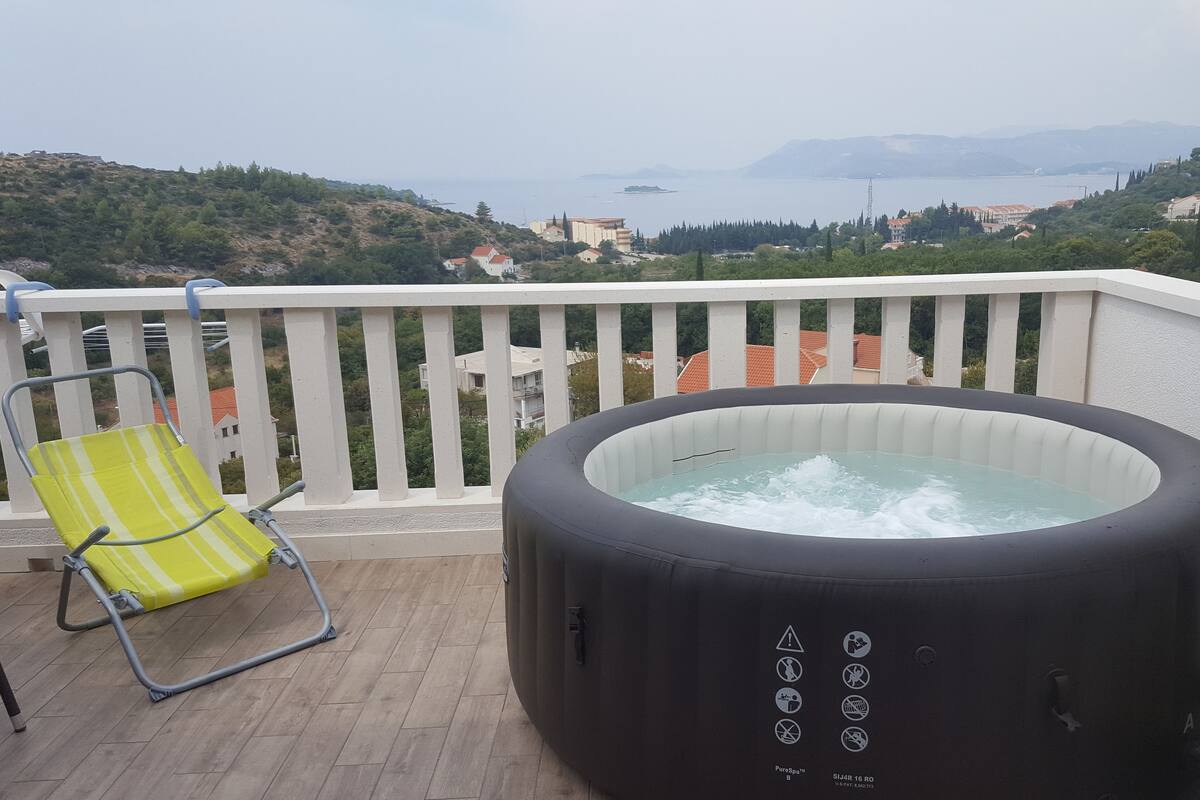 A hot tub on a balcony with a view of the sea and hills.