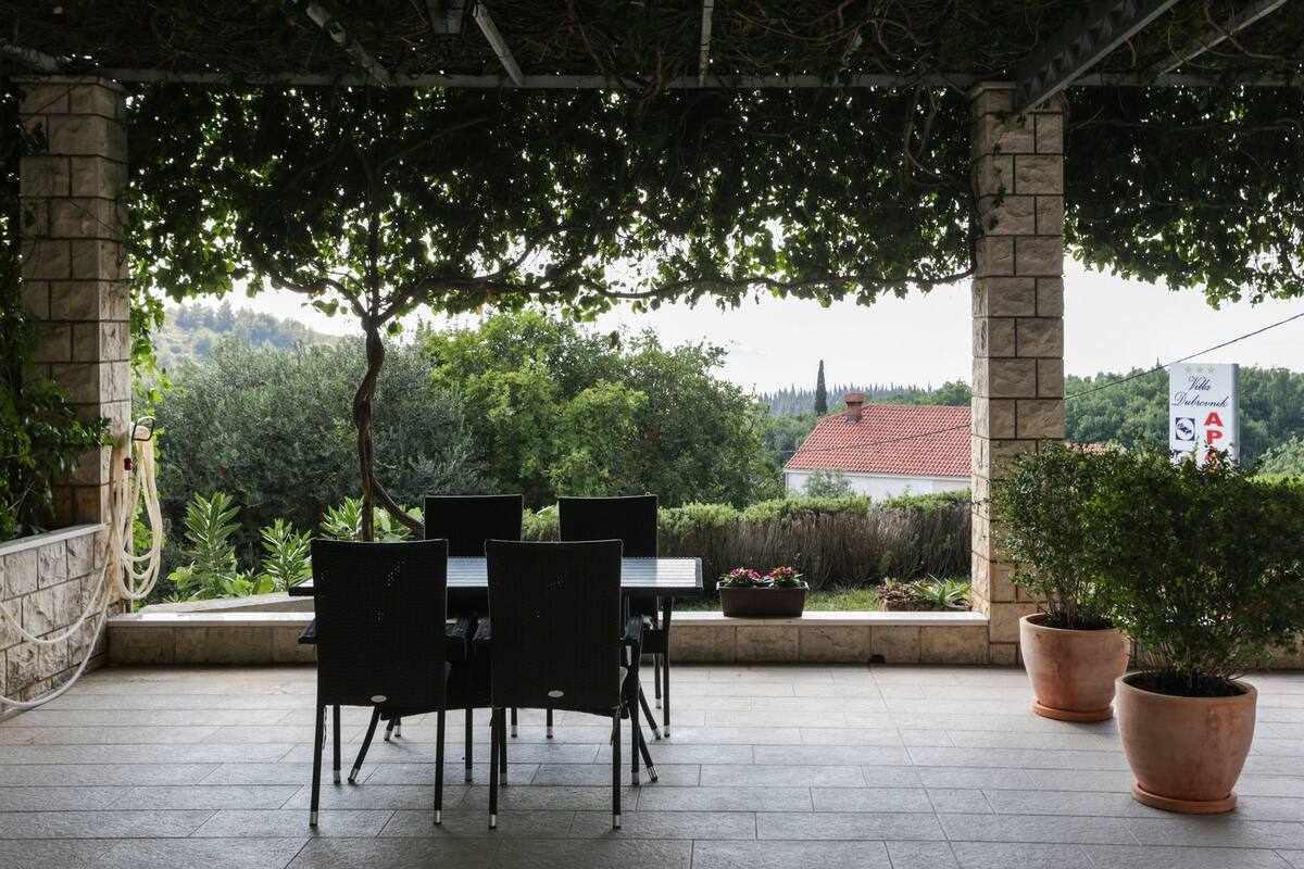 An outdoor patio with stone columns, black chairs, and potted plants.
