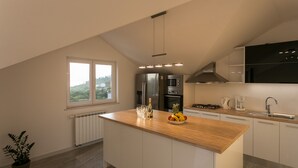 A modern kitchen with a wooden island, stainless steel appliances, and a view of greenery outside. - Apartments Villa Dubrovnik (Konavle)