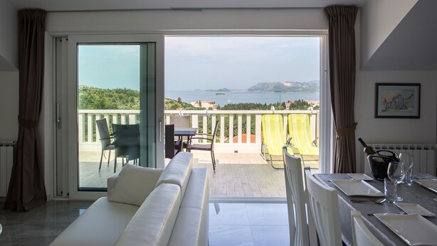 A modern room with a balcony, a sofa, a dining table set, and a view of the sea and hills. - Apartments Villa Dubrovnik (Konavle)