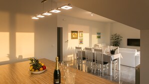 A modern dining area with a wooden table, white chairs, and a white sofa in the background. - Apartments Villa Dubrovnik (Konavle)