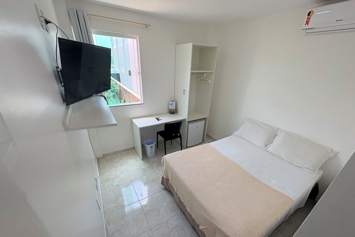Quarto com cama, escrivaninha, cadeira, televisão e guarda-roupa.
