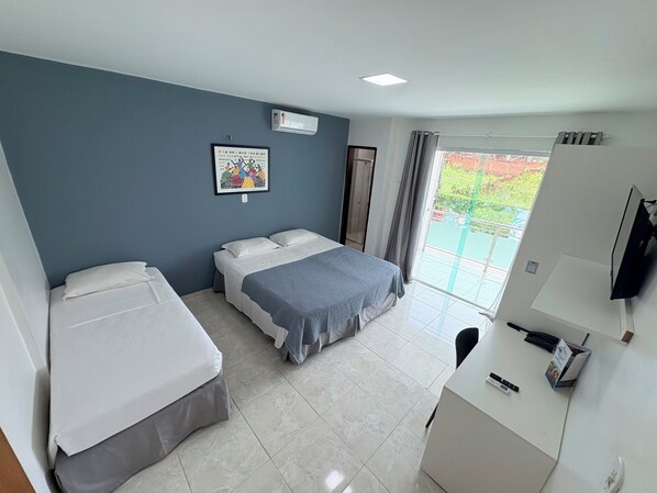 Habitación de hotel con dos camas, un escritorio con teléfono y control remoto, un televisor, una ventana con vistas a zonas verdes y un equipo de aire acondicionado en la pared.