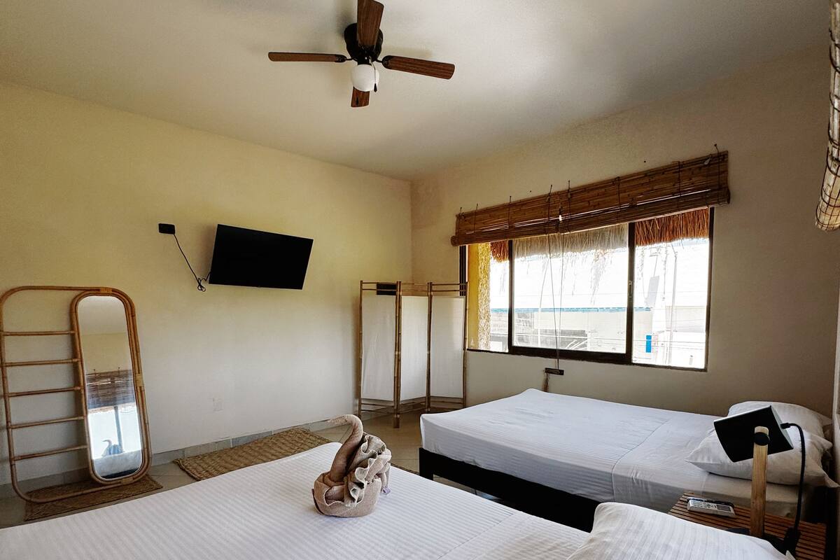 A hotel room with two beds, a ceiling fan, a TV mounted on the wall, and a window with a view.