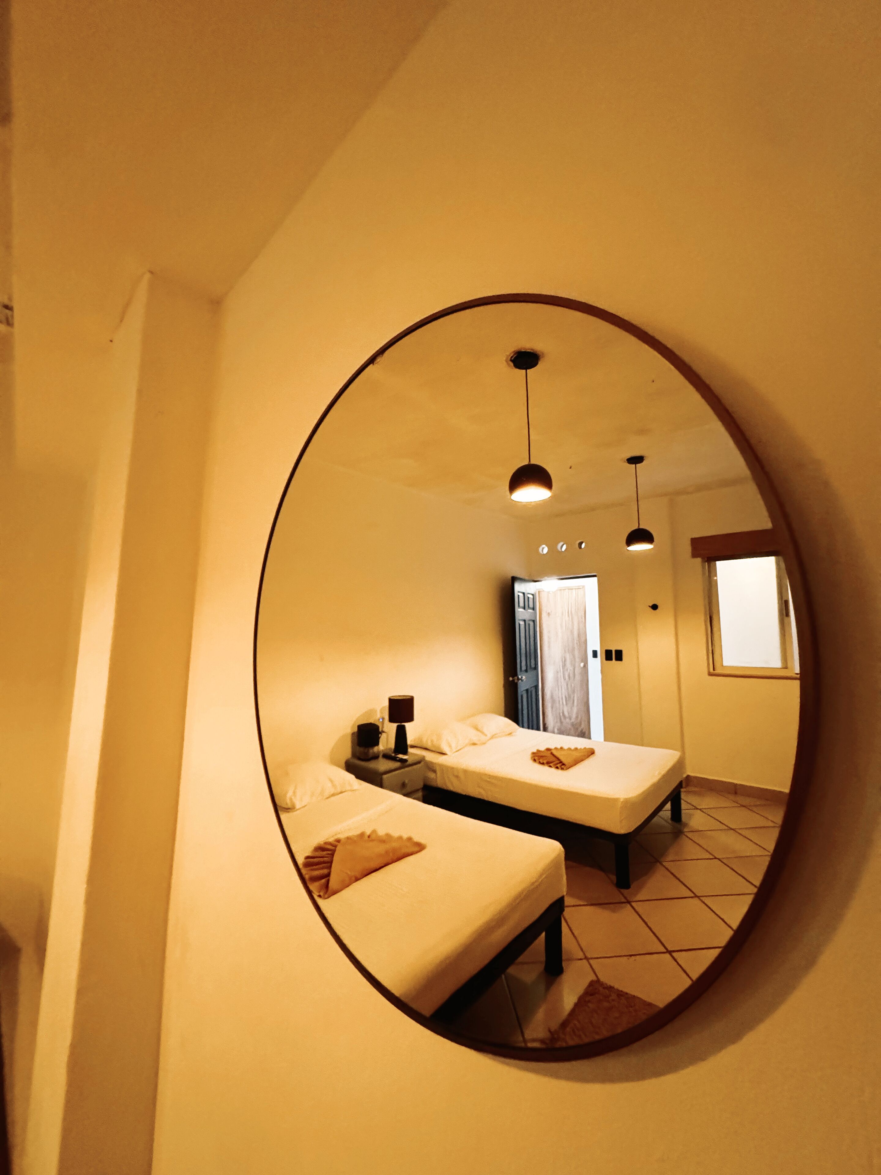 A bedroom with two beds, a round mirror, and a window.