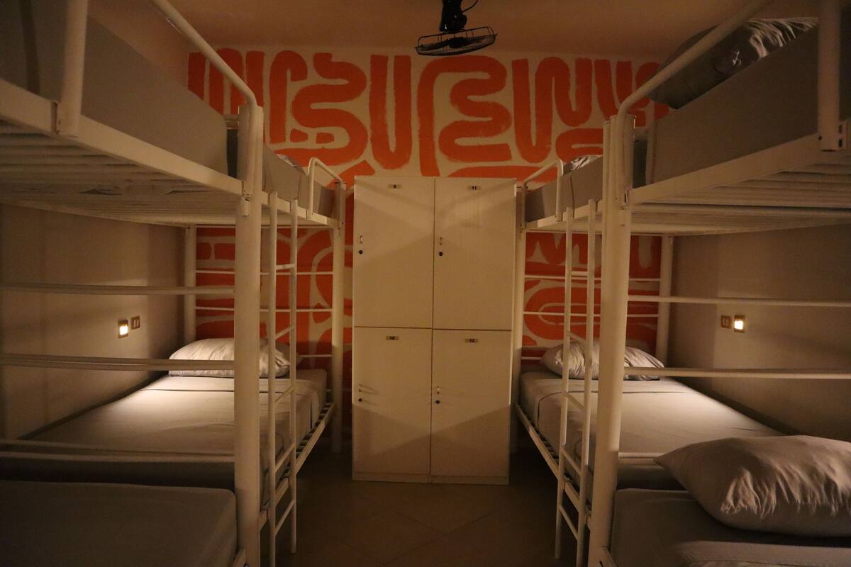 A dormitory room with bunk beds, a wardrobe, and a wall with orange patterns.