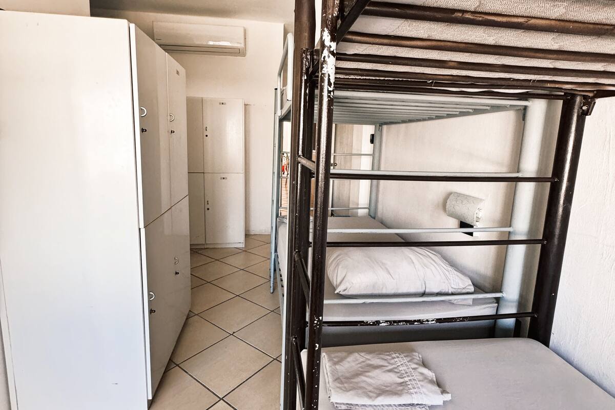 A bunk bed with a mattress and pillows, a white refrigerator, and a tiled floor.