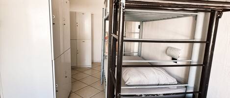 A bunk bed with a mattress and pillows, a white refrigerator, and a tiled floor.