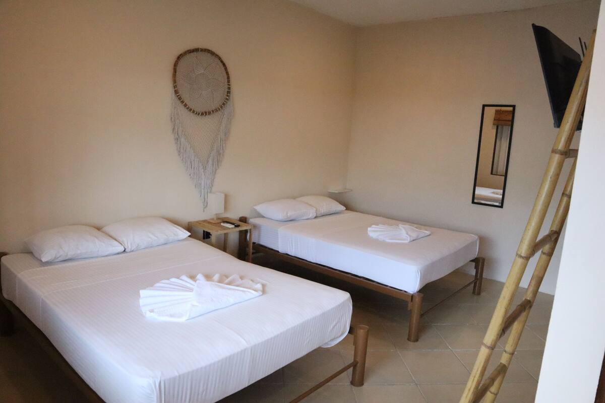 A hotel room with two beds, a bedside table, a dreamcatcher, and a mirror on the wall.