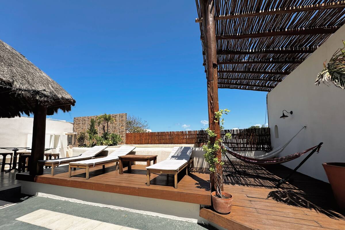 A rooftop terrace with lounge chairs, a hammock, and a thatched roof structure.