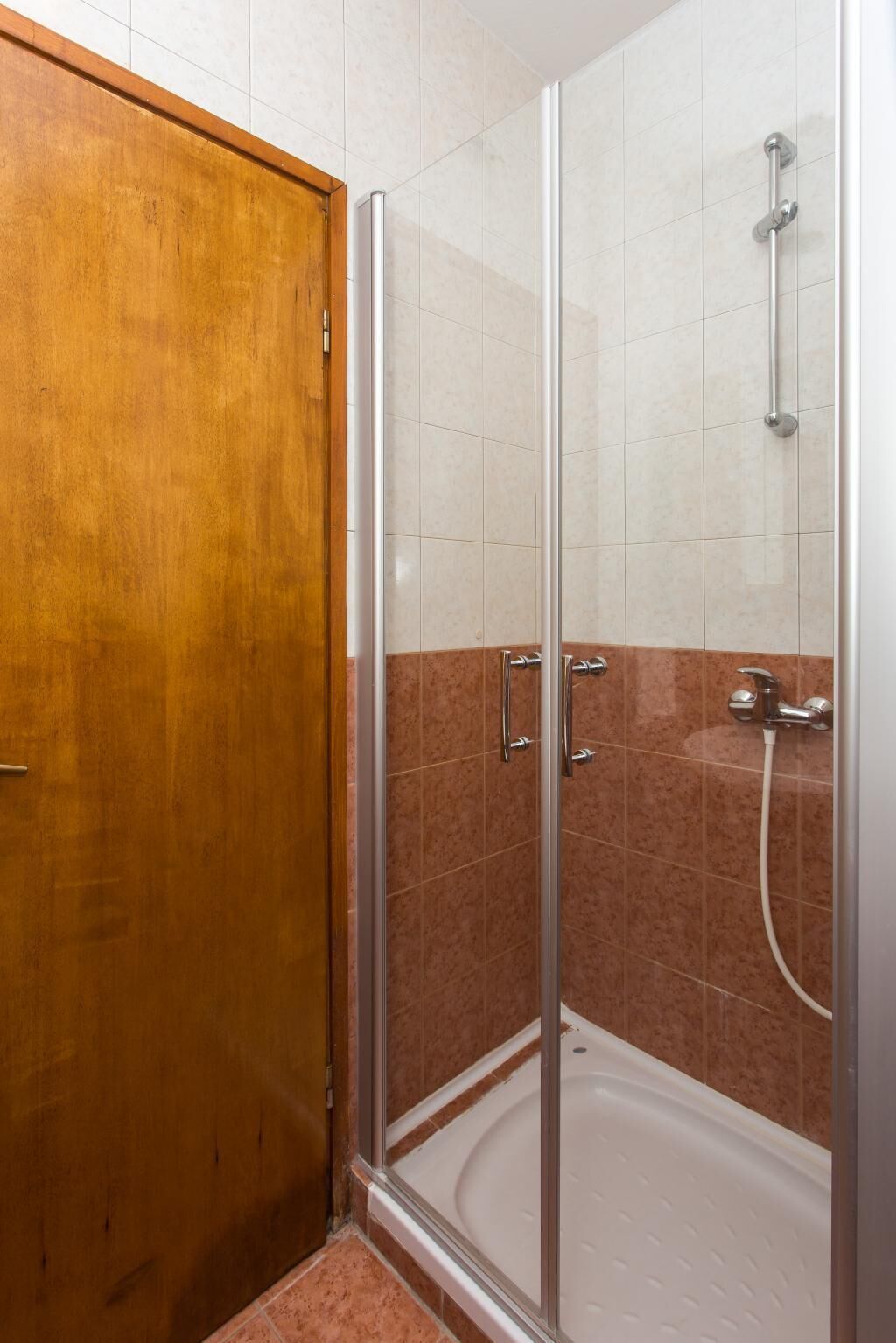 A shower area with a glass door, a bathtub, and a wooden door.
