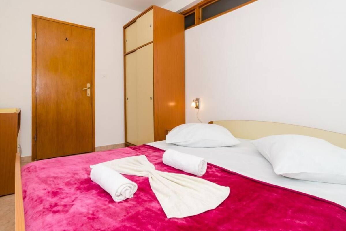 Habitación de hotel con una cama, dos almohadas blancas, una colcha roja y dos toallas enrolladas sobre la cama.