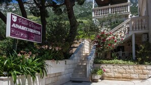 Une villa avec une enseigne indiquant qu’elle propose des appartements, un escalier en pierre et une végétation luxuriante.