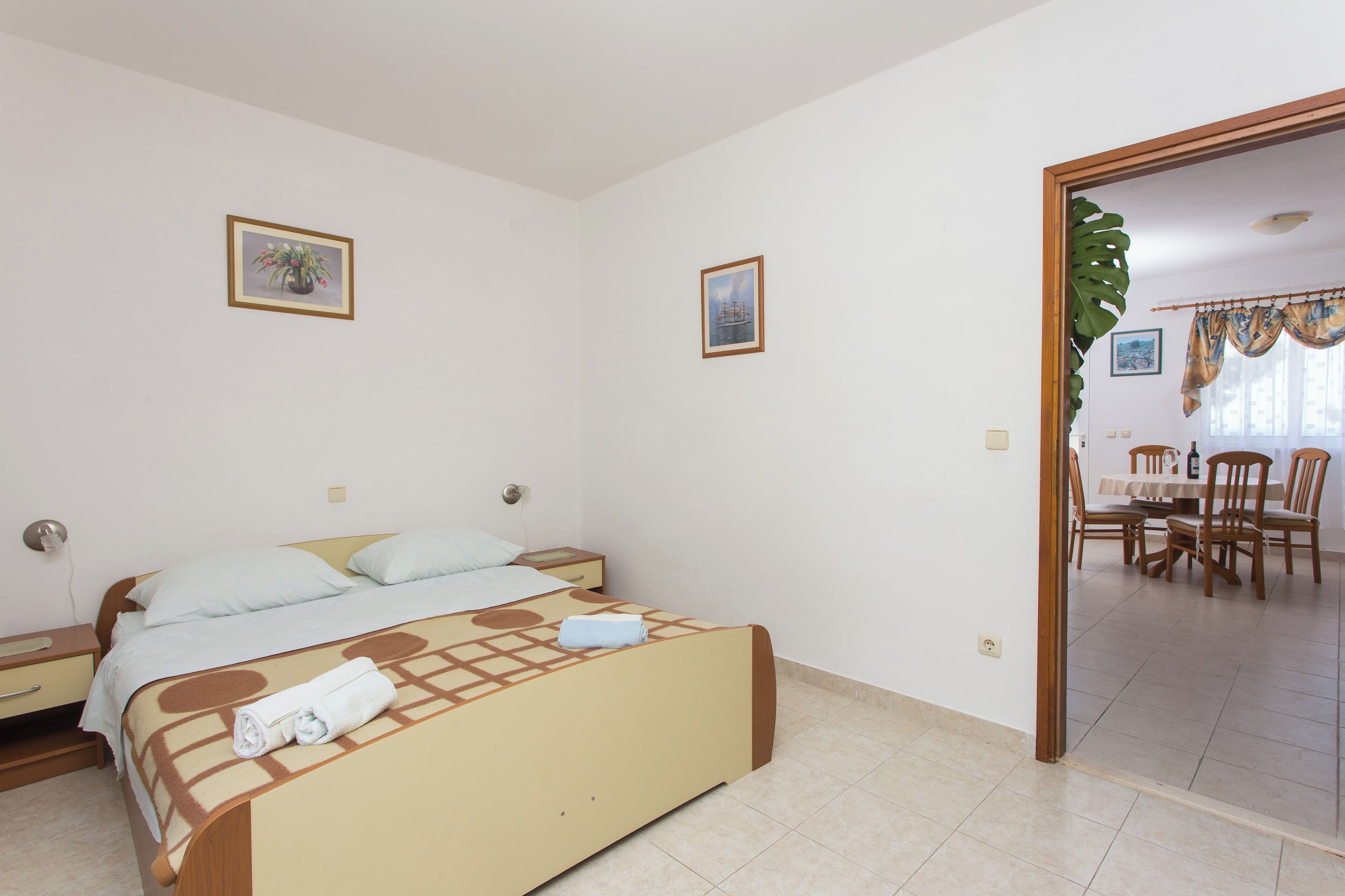 A bedroom with a bed, a nightstand, a chair, and a dining area with a table and chairs.