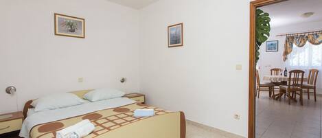 A bedroom with a bed, a nightstand, a chair, and a dining area with a table and chairs.