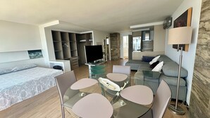 A modern living room with a glass dining table, grey sofa, and a TV in the background.