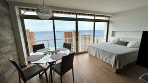 A modern bedroom with a large window, a round dining table with chairs, and a bed with a headboard.
