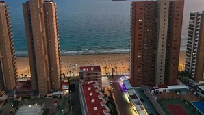 A high-rise hotel with a beach view, multiple balconies, and a swimming pool area.