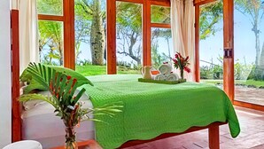 A room with a bed, a small table with towels and a vase, and large windows with a view of trees. - Ocean Properties Aparthotel Villas (Punta Mala)