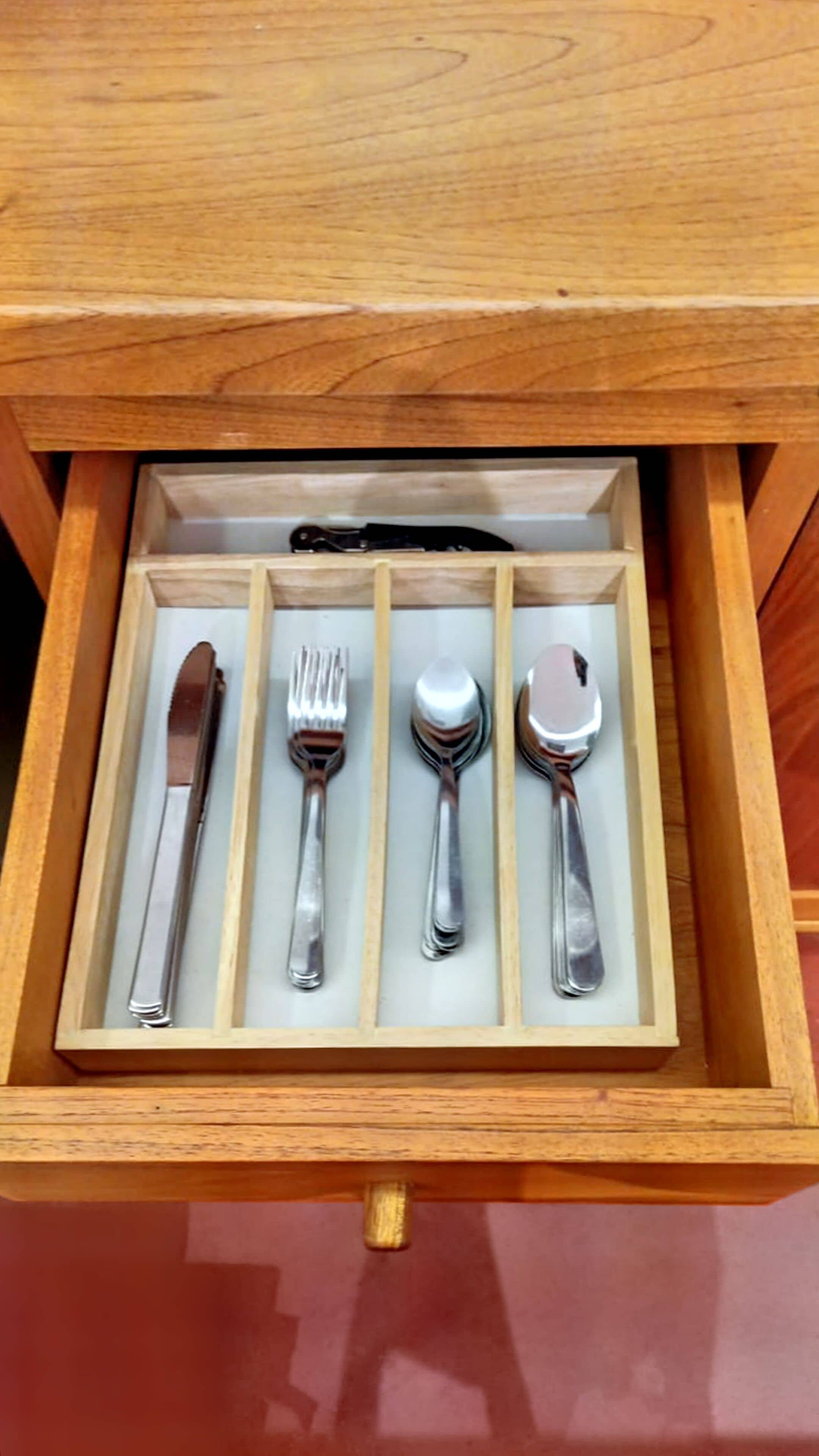 Un cajón de madera con compartimentos que contienen un cuchillo, un tenedor, una cuchara y otra cuchara con mango.