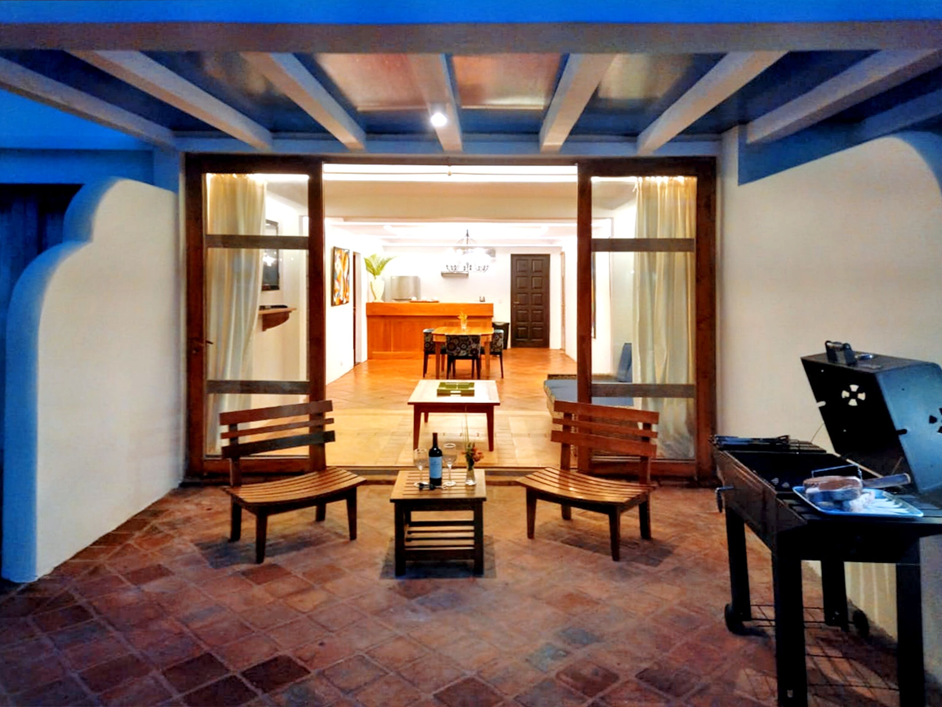 A cozy patio area with wooden furniture, a grill, and a view into the dining room.
