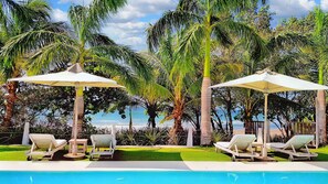 A poolside area with lounge chairs and umbrellas, surrounded by palm trees and a view of the ocean. - Ocean Properties Aparthotel Villas (Punta Mala)