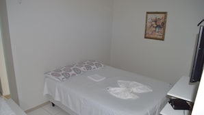A single-bed room with a white bedspread, a patterned pillow, a small bedside table, and a wall-mounted TV. - Loura Pousada (Sobral)