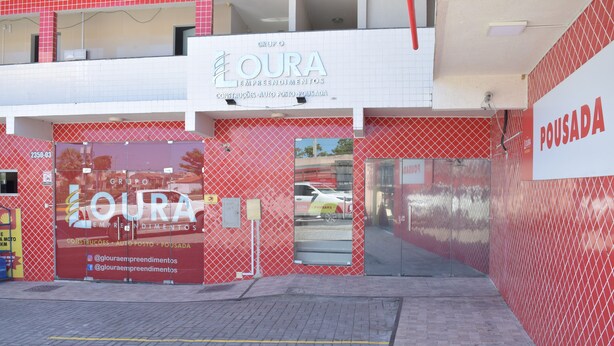 A commercial building with a red and white facade, featuring a large sign for 'LOURA EMPREENDIMENTOS' and a smaller sign for 'POUSADA'. - Loura Pousada (Sobral)