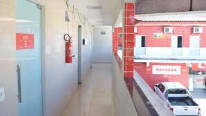 A corridor with a fire extinguisher, a sign reading "SAIDA", and a red wall with "POUSADA" written on it. - Loura Pousada (Sobral)